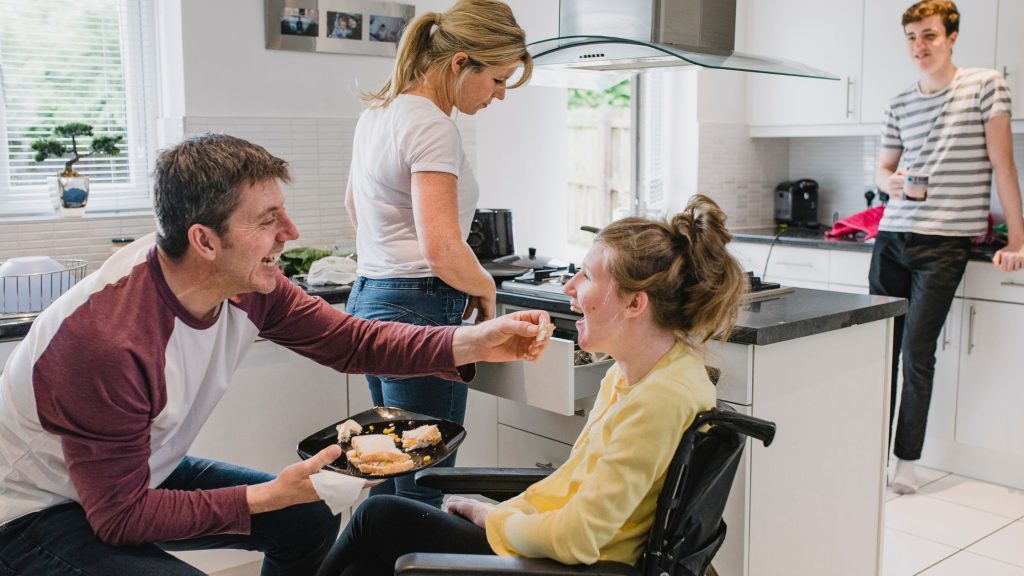 A lady in a wheelchair being assisted in her kitchen.